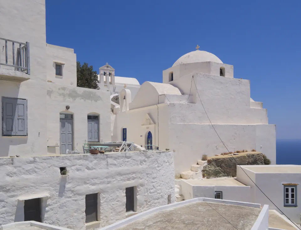 Λευκά σπίτια και λευκή εκκλησία με τρούλο στη Χώρα της Σερίφου, με τη θάλασσα δεξιά και καθαρό γαλάζιο ουρανό.