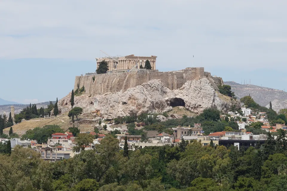 Ο βράχος της Ακρόπολης με τον Παρθενώνα πάνω από τα δέντρα και τα σπίτια της Αθήνας.