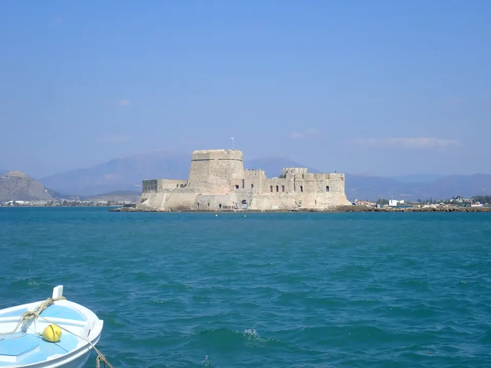 Το κάστρο Μπούρτζι στη θάλασσα του Ναυπλίου, με ένα μικρό γαλάζιο καΐκι στο πρώτο πλάνο.